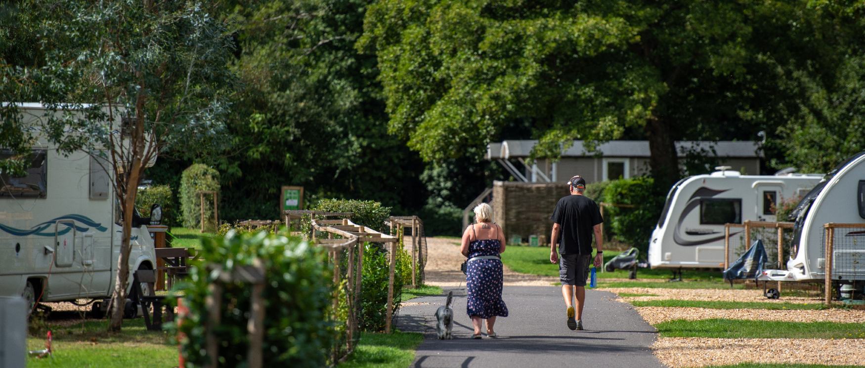 A couple and their dog walk through Back of Beyond Touring, Camping & Glamping Park